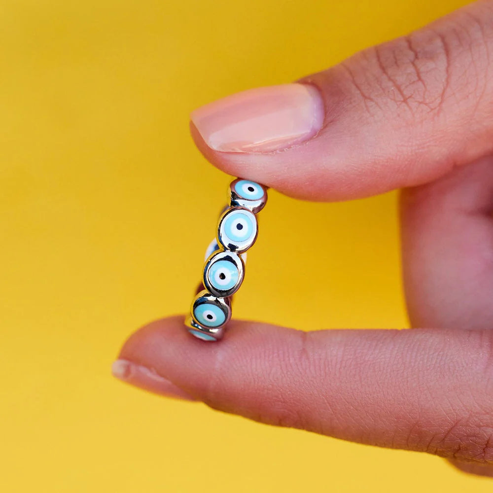 Hand holding a small decorative item with blue eyes against a yellow background
