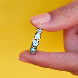 Hand holding a small decorative item with blue eyes against a yellow background