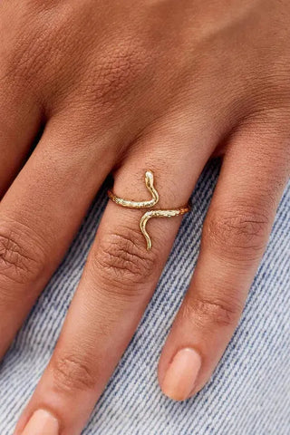 Gold snake-shaped ring on a person's finger with a denim background