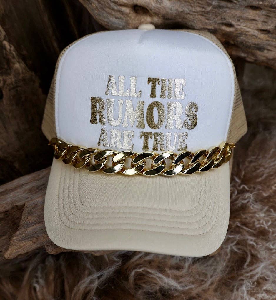 Beige cap with 'All the rumors are true' text and gold chain on a wooden surface