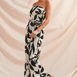 Woman wearing a strapless black and white patterned jumpsuit against a beige backdrop