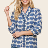 Woman wearing a blue and white patterned blouse with jeans on a beige background