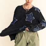 Person wearing a black sweater with star-shaped cutouts and green pants on a beige background