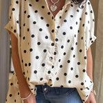 Person wearing a beige shirt with black polka dots and blue jeans indoors.