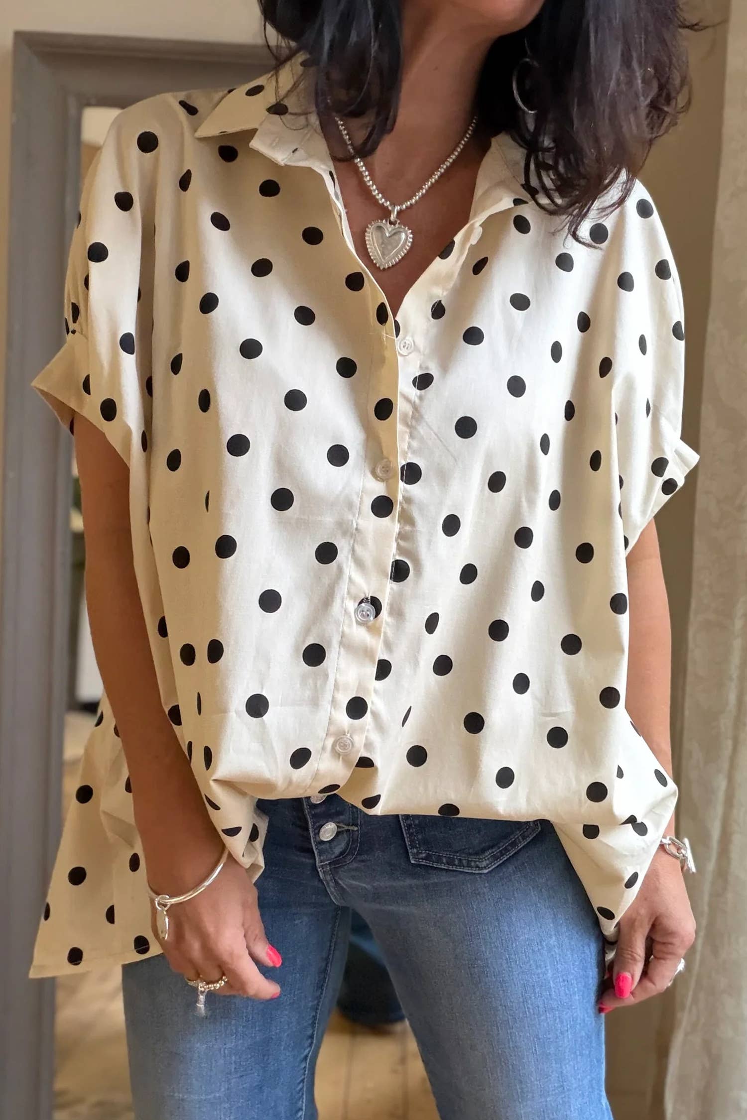 Person wearing a beige shirt with black polka dots and blue jeans indoors.