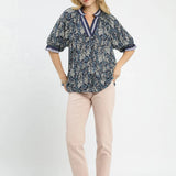 Woman wearing a navy floral blouse and beige pants on a white background