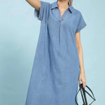 Woman wearing a light blue denim dress holding a woven bag on a light blue background