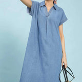Woman wearing a light blue denim dress holding a woven bag on a light blue background