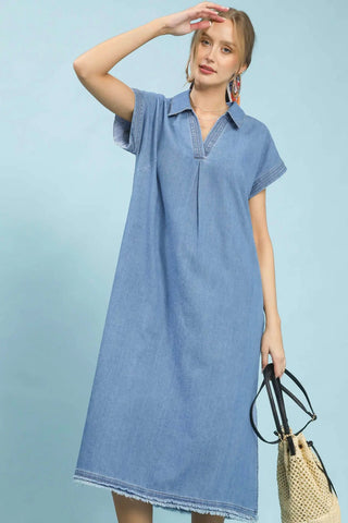 Woman wearing a light blue denim dress holding a woven bag on a light blue background