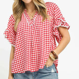 Woman wearing a red and white checkered blouse with denim shorts on a white background