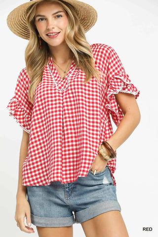 Woman wearing a red and white checkered blouse with denim shorts on a white background