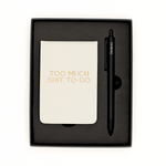Notebook with 'Too Much Shit To Do' text and a pen in a black box on a white background