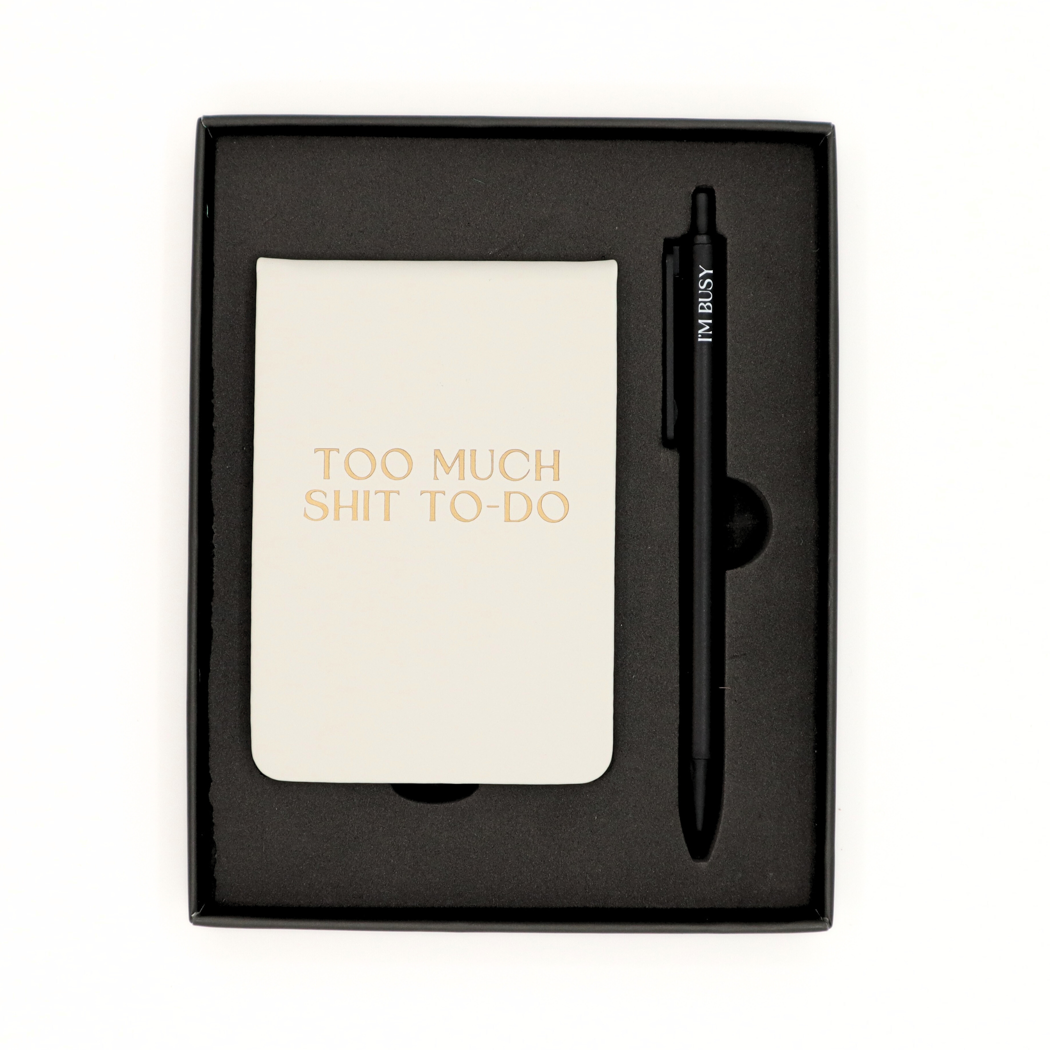 Notebook with 'Too Much Shit To Do' text and a pen in a black box on a white background