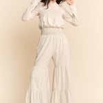 Woman wearing a white outfit with ruffled pants against a beige background