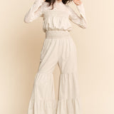 Woman wearing a white outfit with ruffled pants against a beige background