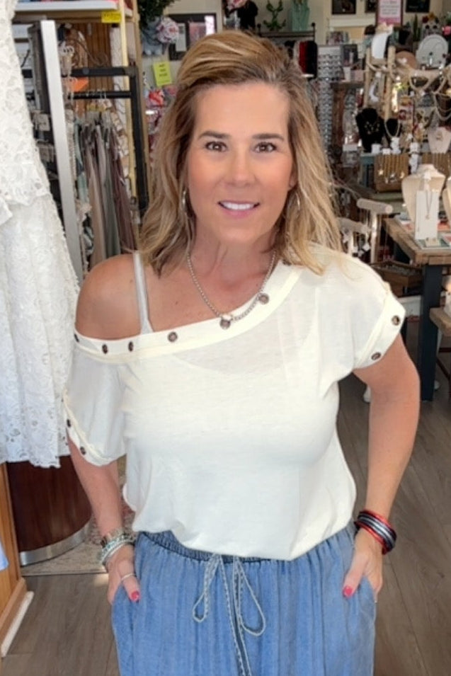 Woman in a store wearing a white top and blue skirt, surrounded by various items.