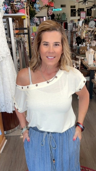 Woman in a store wearing a white top and blue skirt, surrounded by various items.