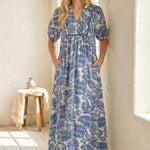 Woman wearing a blue floral dress standing in a bright room with wooden floor and white walls.