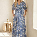 Woman wearing a blue floral dress standing in a bright room with wooden floor and white walls.