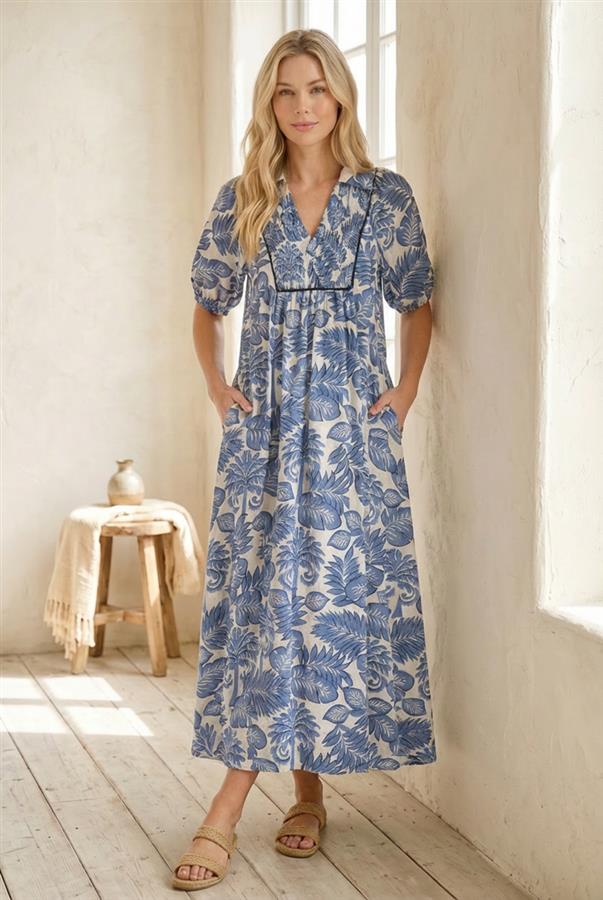 Woman wearing a blue floral dress standing in a bright room with wooden floor and white walls.