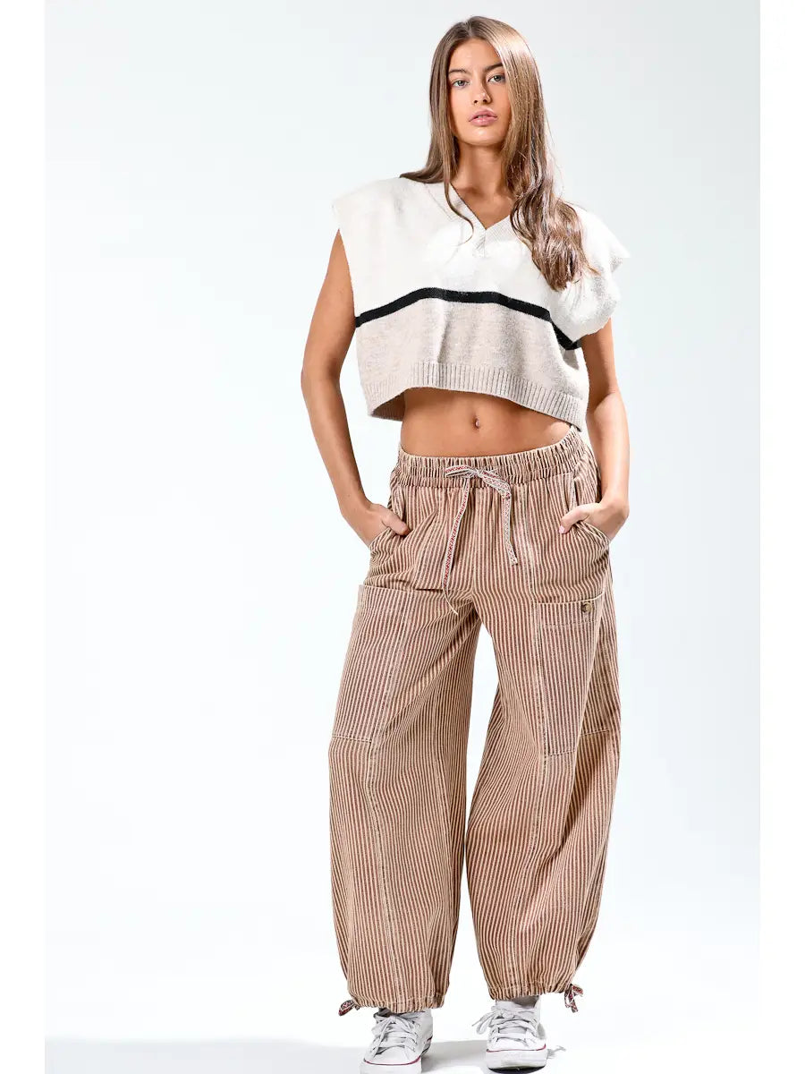 Woman wearing a white sleeveless top with black trim and beige striped pants on a white background