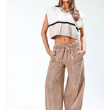 Woman wearing a white sleeveless top with black trim and beige striped pants on a white background