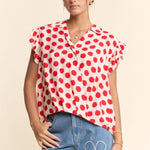 Woman wearing a red and white polka dot blouse with blue jeans featuring floral designs on a beige background