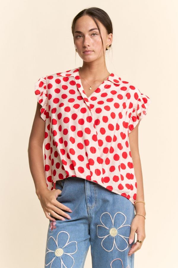 Woman wearing a red and white polka dot blouse with blue jeans featuring floral designs on a beige background