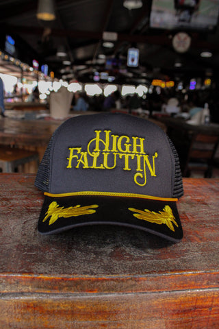 Black and yellow cap with 'High Falutin' text on a wooden surface in a bar setting