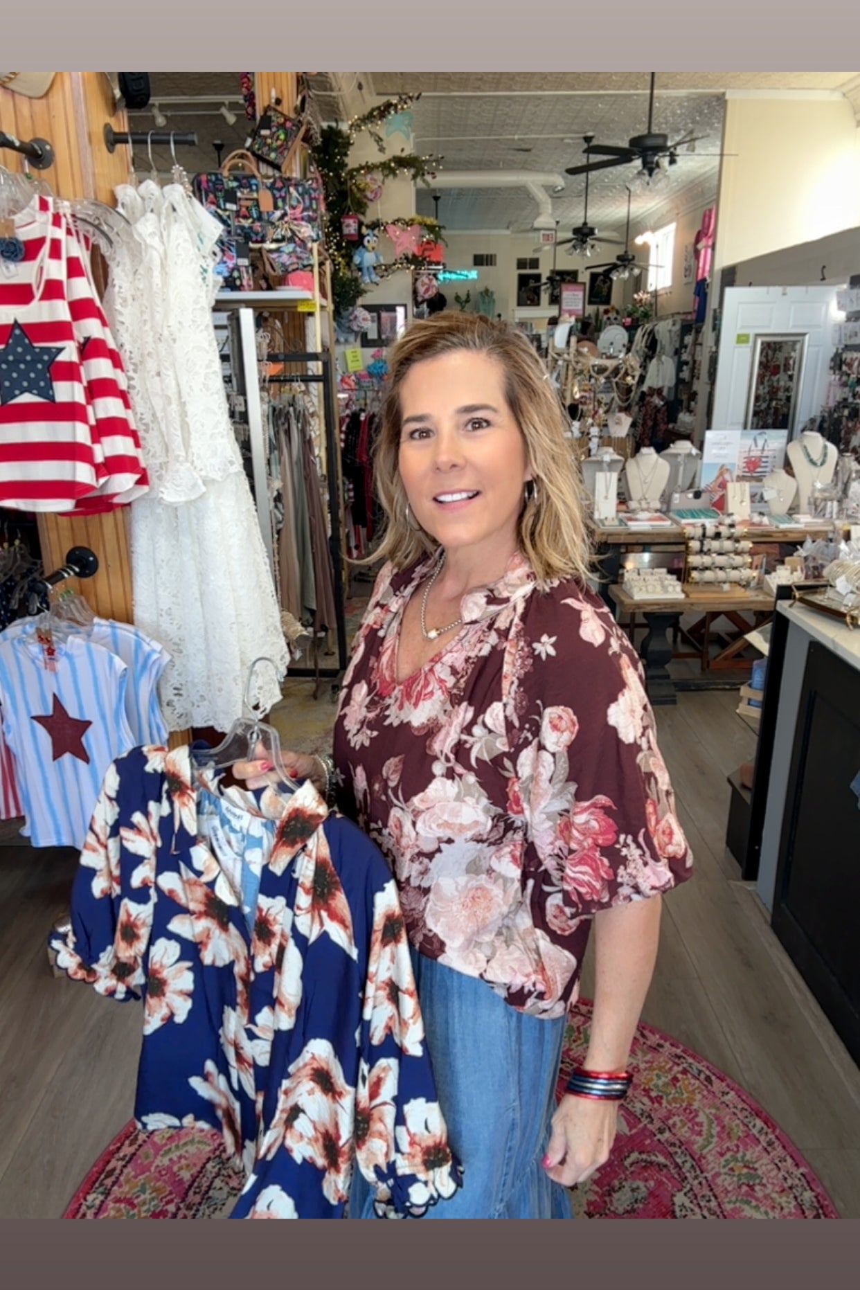 Woman standing in a store with clothing racks and American flag in the background