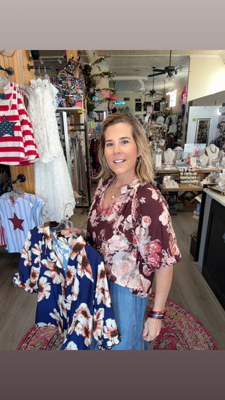 Woman standing in a store with clothing racks and American flag in the background