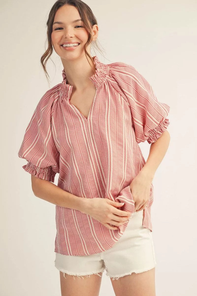 Woman wearing a red and white checkered blouse with ruffled sleeves on a plain background