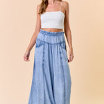 Woman wearing a white top and blue denim skirt on a beige background