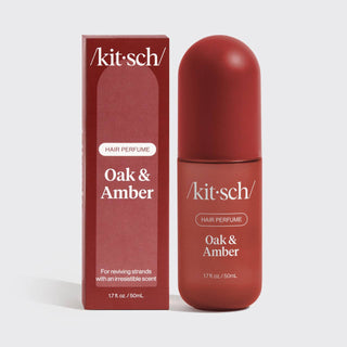 A bottle of Kit Sch Hair Perfume Oak & Amber next to its matching box packaging, both in a deep reddish-brown shade, on a light gray background.