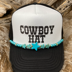 Black and white trucker hat with 'Cowboy Hat' text and turquoise beaded band on a wooden background
