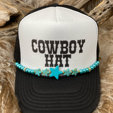 Black and white trucker hat with 'Cowboy Hat' text and turquoise beaded band on a wooden background