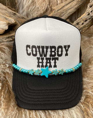 Black and white trucker hat with 'Cowboy Hat' text and turquoise beaded band on a wooden background