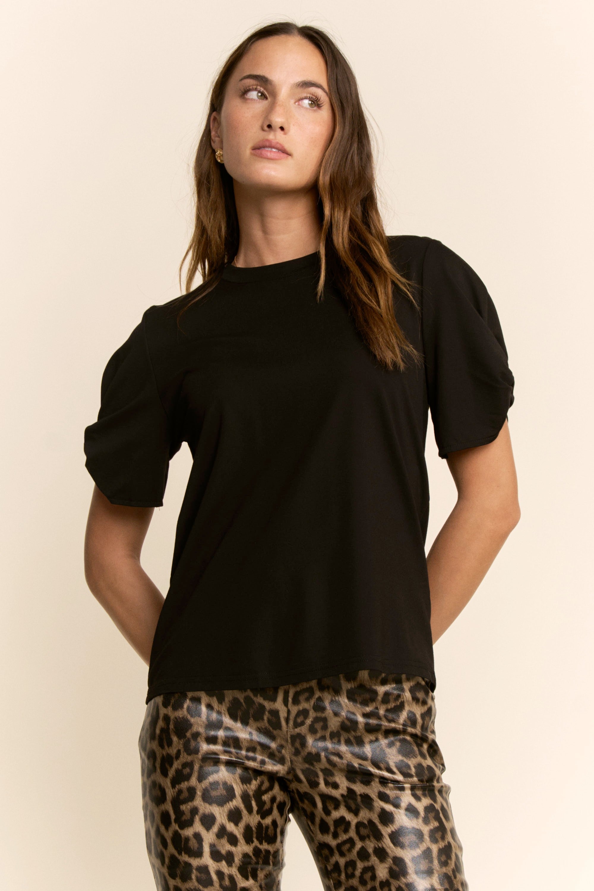 Woman wearing a black top and leopard print pants on a beige background