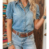 Woman wearing a denim shirt and jeans with a belt, standing in a room with wooden walls.