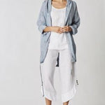Woman wearing a light blue jacket and white pants on a plain background