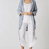 Woman wearing a light blue jacket and white pants on a plain background