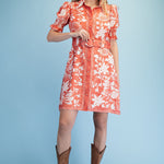 Woman wearing a red floral dress and brown cowboy boots on a light blue background