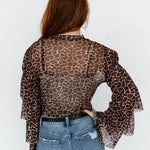 Person wearing a leopard print sheer top and blue jeans on a white background