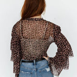 Person wearing a leopard print sheer top and blue jeans on a white background