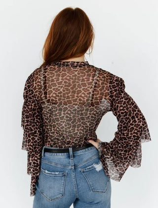 Person wearing a leopard print sheer top and blue jeans on a white background