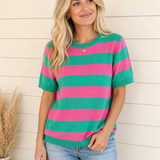 Woman wearing a pink and green striped shirt against a wooden wall.