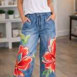 Woman wearing floral denim pants and a white shirt in a room.
