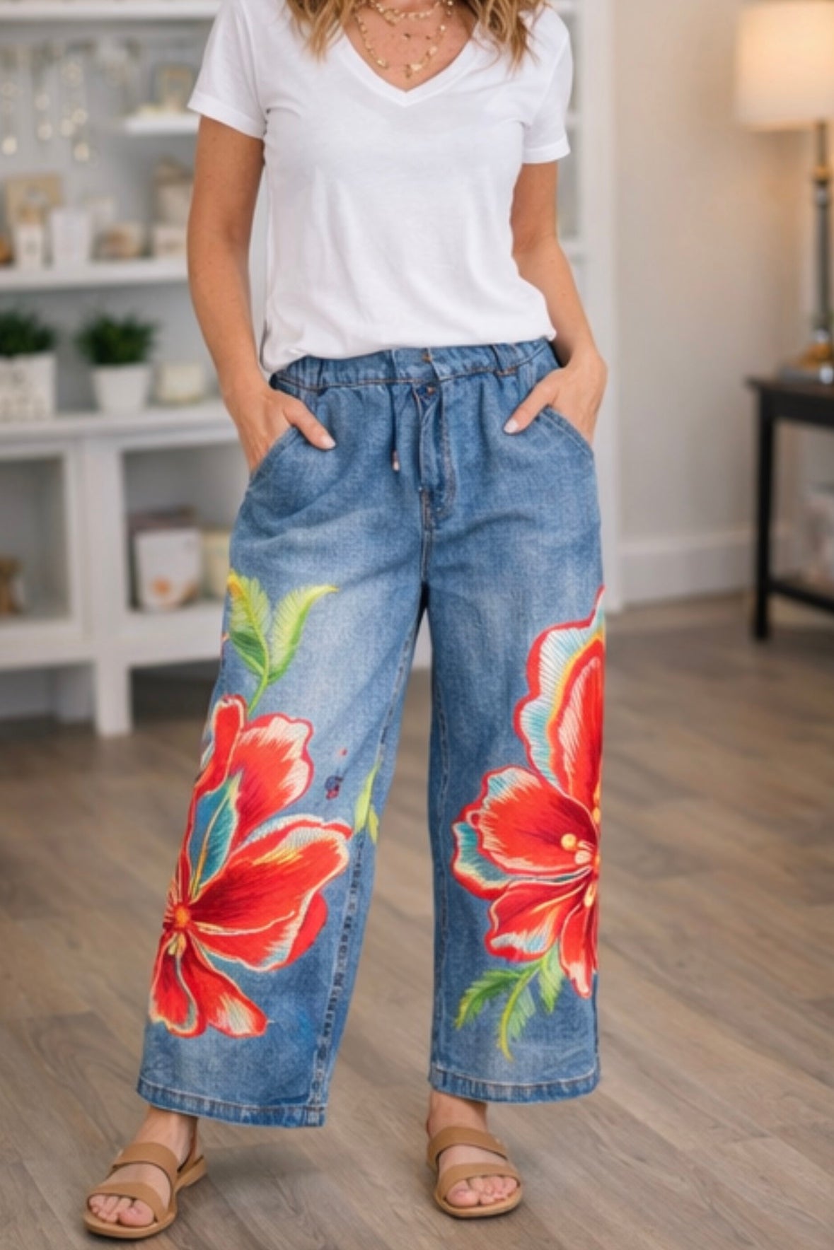 Woman wearing floral denim pants and a white shirt in a room.