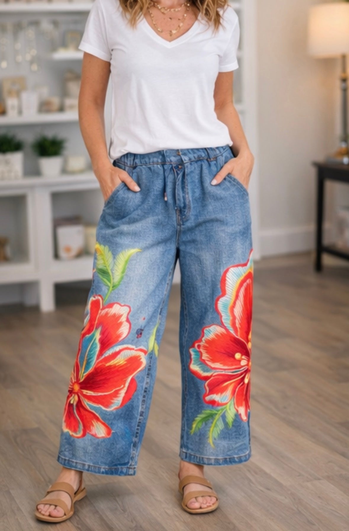 Woman wearing floral denim pants and a white shirt in a room.