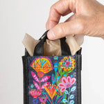 Hand holding a small black bag with colorful floral designs on a light gray background